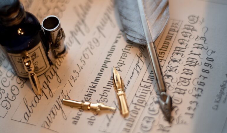 Macro shot of a quill set and an ink bottle on a piece of paper with calligraphy on it